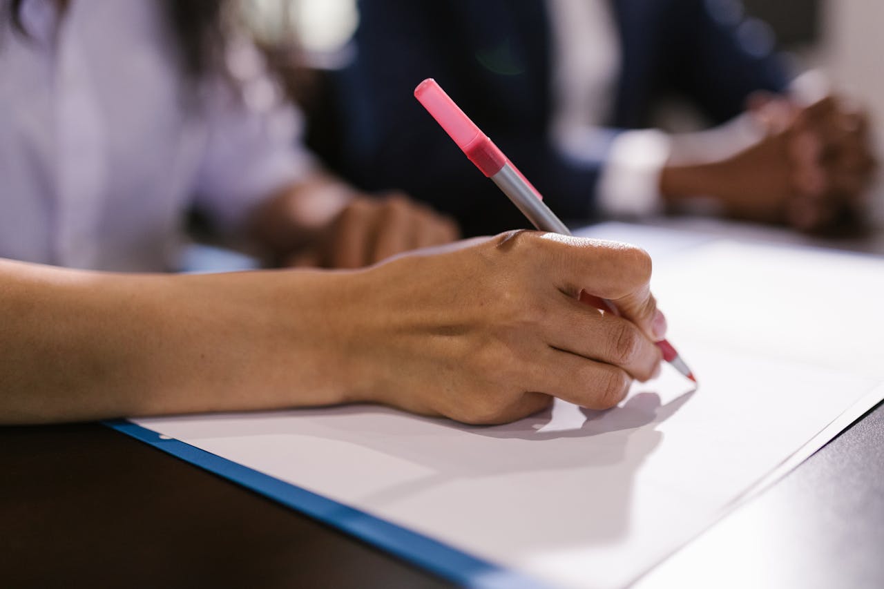 Detailed close-up of a person writing on paper with a pen in an office setting.
